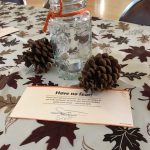 Thanksgiving dinner place-setting; tealight candle, mason jar, pinecones and a tablecloth with fall foliage