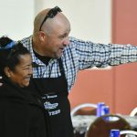 A smiling volunteer cheerfully guides a couple into the dining hall
