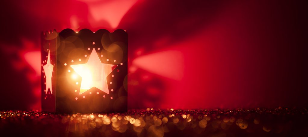 A tealight lattern with a star pattern sitting on shiny sequens glows against a red background