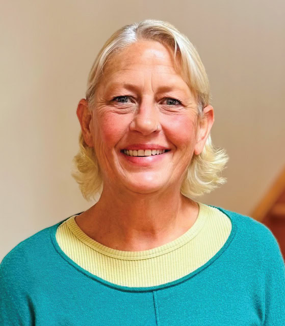 Smiling woman with blonde hair wearing a teal and yellow top.