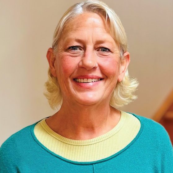 Smiling woman with blonde hair wearing a teal and yellow top.