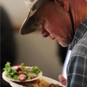 A homeless man eyes his meal, paper plates carefully balanced