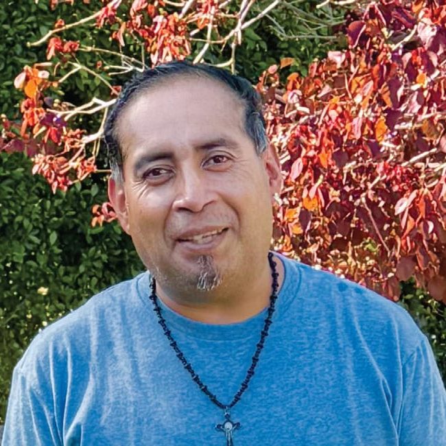 Rescue Mission Alliance Central Coast volunteer smiling outdoors with colorful foliage in background.