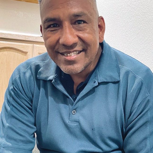 A smiling man in a blue polo shirt at Rescue Mission Alliance Central Coast office.