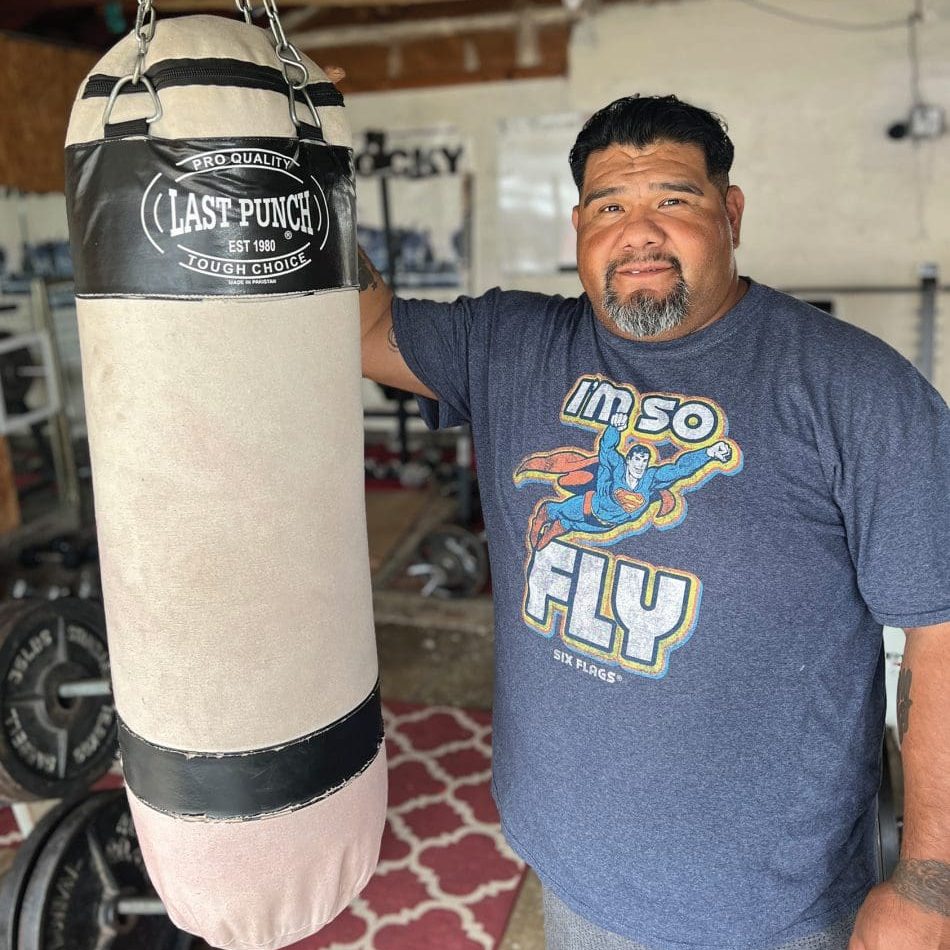 A man, supported by God's grace, stands determined next to a punching bag.